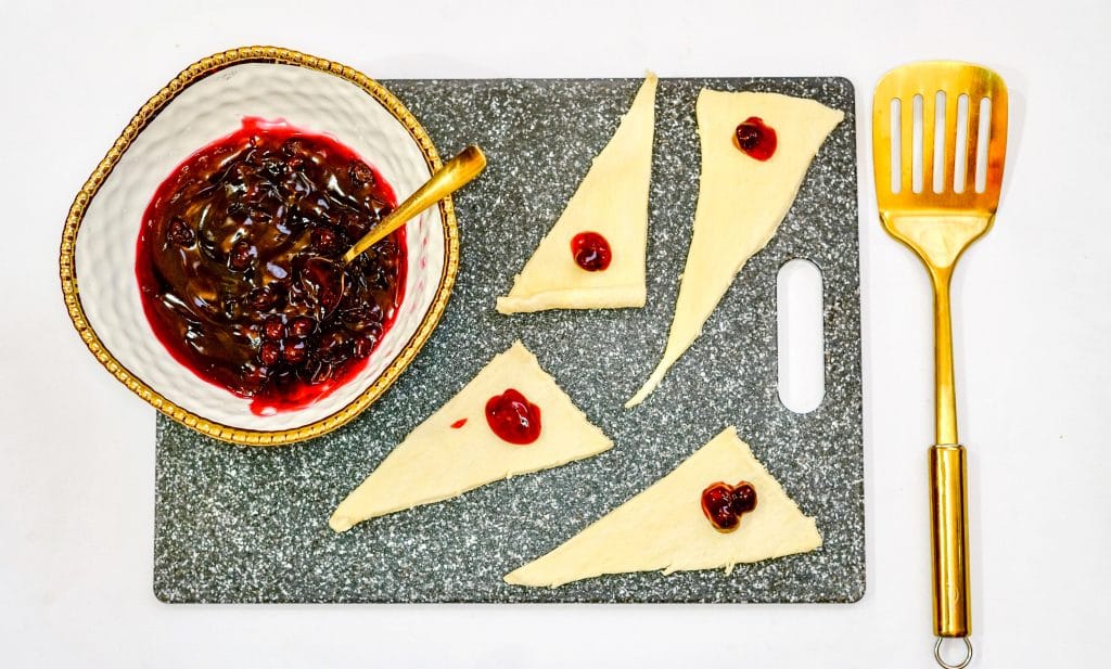 Blueberry pie filling being added to crescent rolls. Step One of Air Fryer Blueberry Dessert Recipe that is made with crescent rolls, blueberry pie filling, cooking spray and powdered sugar.